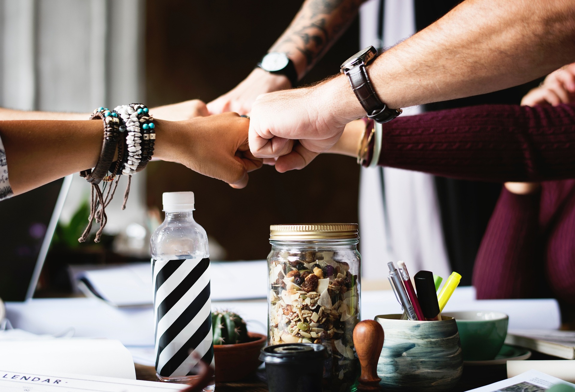 Several hands meeting together over a desk fist bumping each other